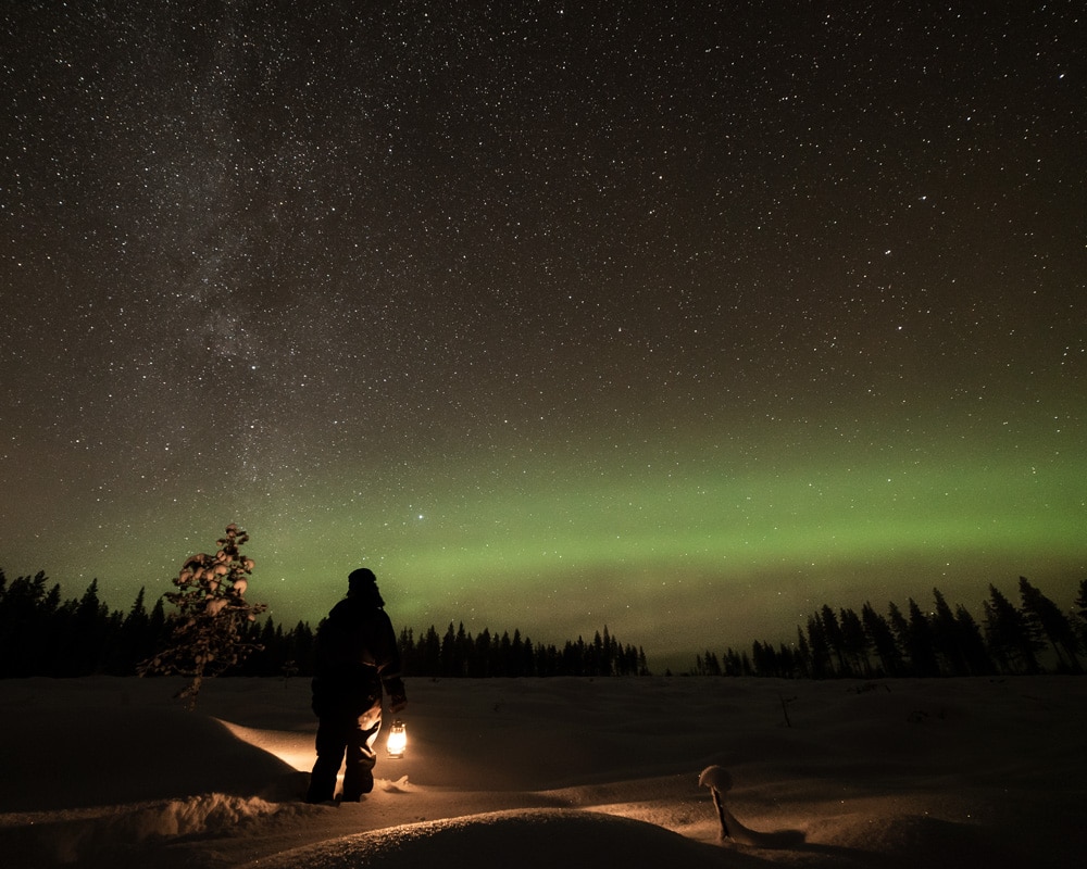 Woman with lantern looking at the milkyway and the northern lights.