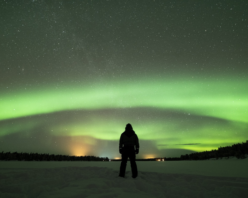22.2.2022 Man standing under the northern lights at Ounasjoki, Finland.