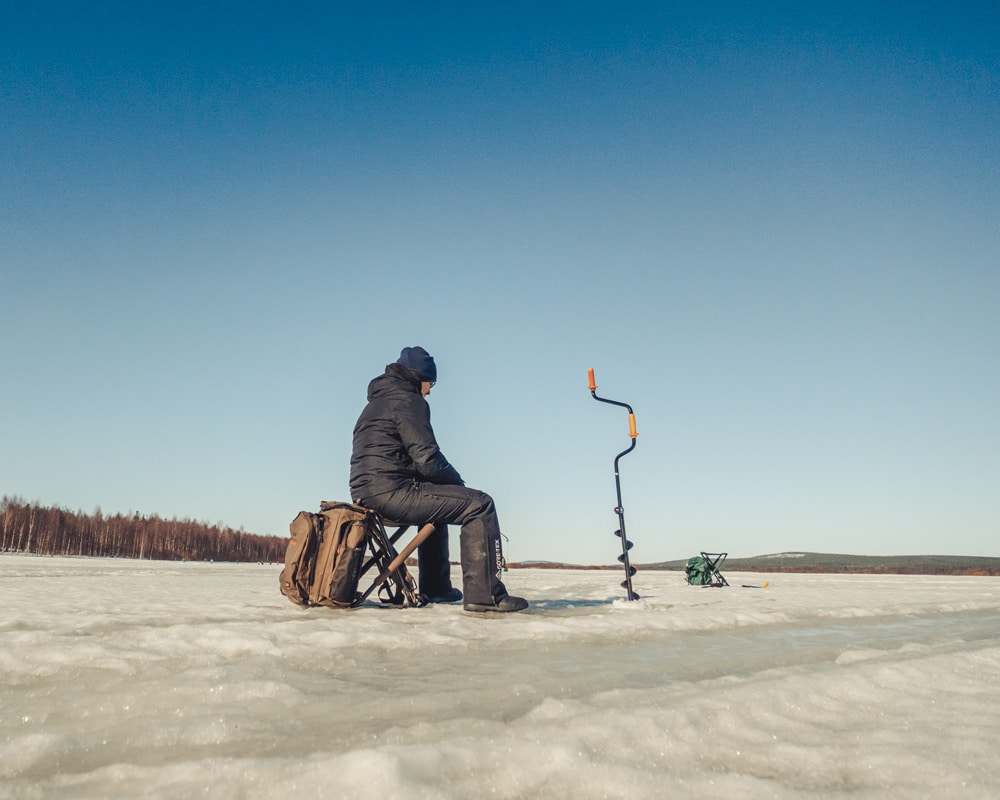 24.3.2022 man ice fishing at Ounasjoki, Finnish Lapland