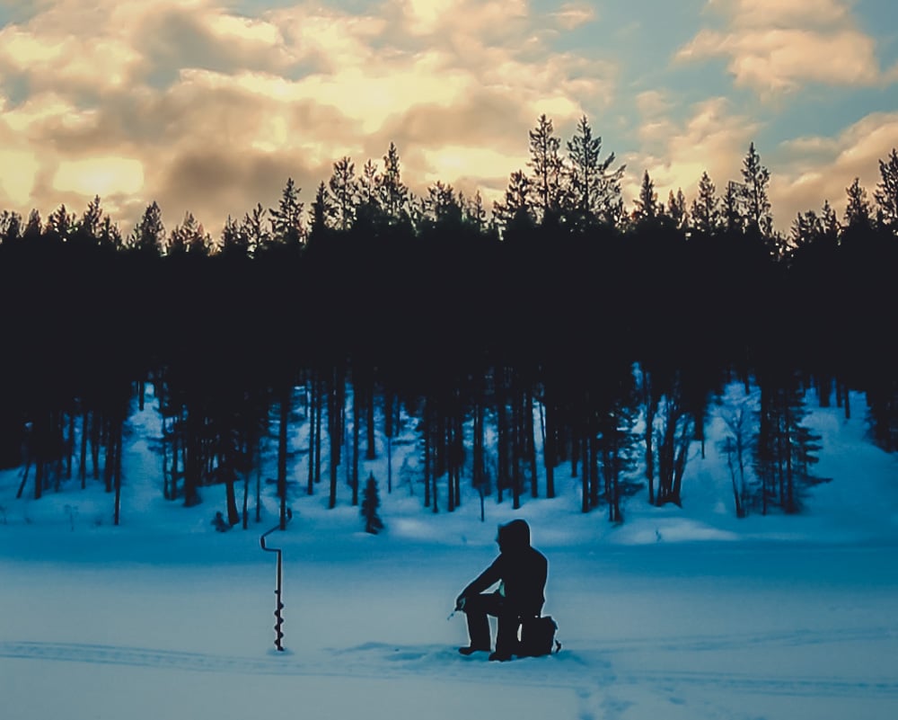 3.4.2020 Man ice fishing in remote lake.