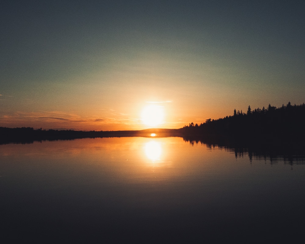 1.6.2020 Midnight sun shines on a still lake at Arctic Circle.
