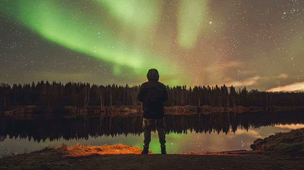 Man standing by the riverside with northern lights.