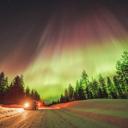 23.3.2023 Car under great northern lights by the roadside in Finnish Lapland.