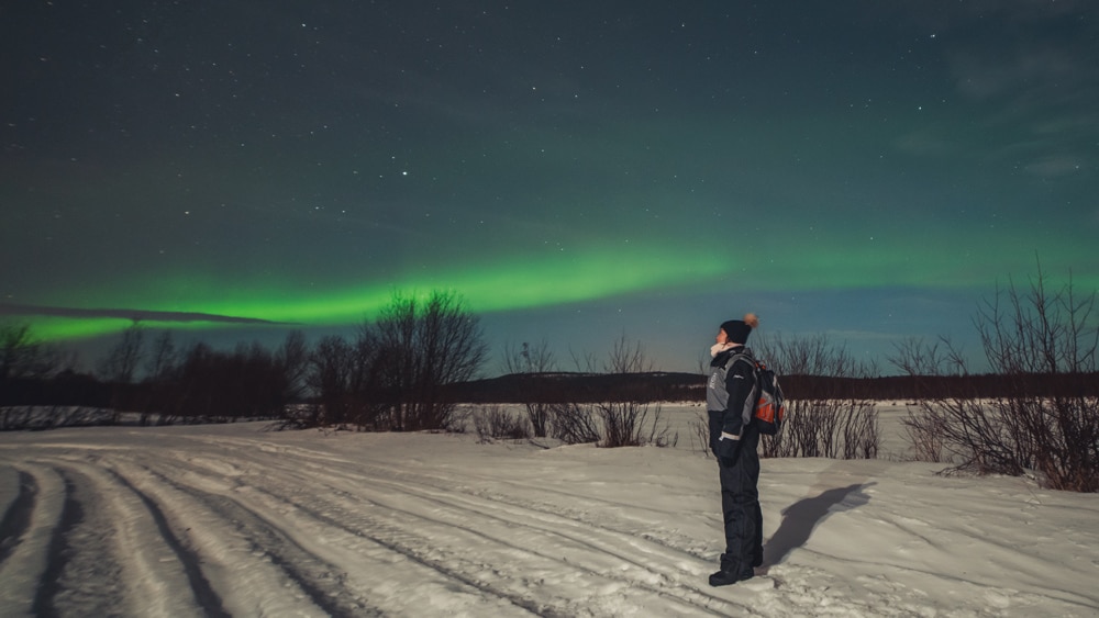 4.1.2020 Woman standing under northern lights in Sinettä, Rovaniemi.