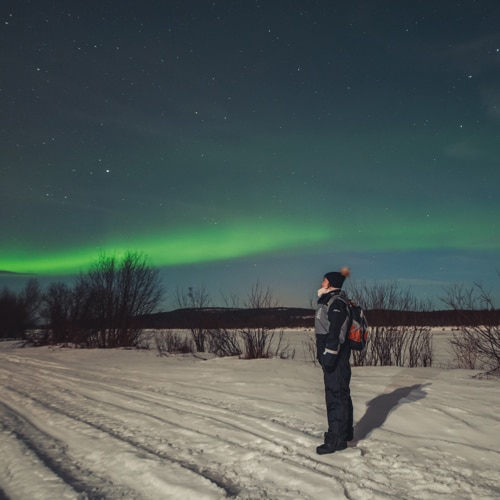 4.1.2020 Woman standing under northern lights in Sinettä, Rovaniemi.